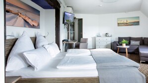 Une chambre d’hôtel moderne avec un grand lit, un canapé, une petite table agrémentée d’une plante et des œuvres d’art accrochées aux murs.
