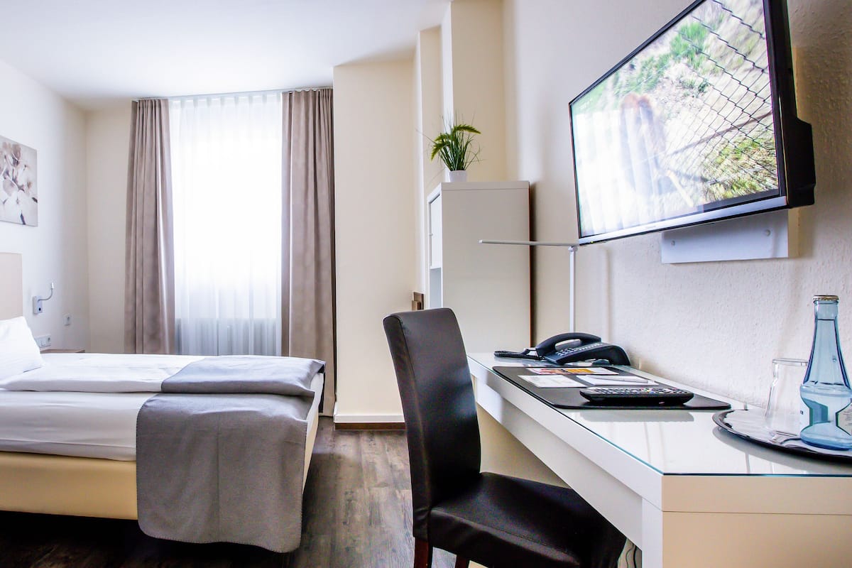 A hotel room with a bed, a desk with a chair, a television, and a window with curtains.