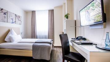 Ein Hotelzimmer mit einem Bett, einem Schreibtisch mit Stuhl, einem Fernseher und einem Fenster mit Vorhängen.