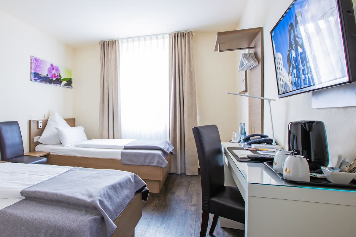 A hotel room with two beds, a desk with a coffee maker, a TV, and artwork on the walls.