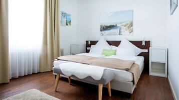 A neatly arranged bedroom with a bed, bedside tables, a window with curtains, and wall art.