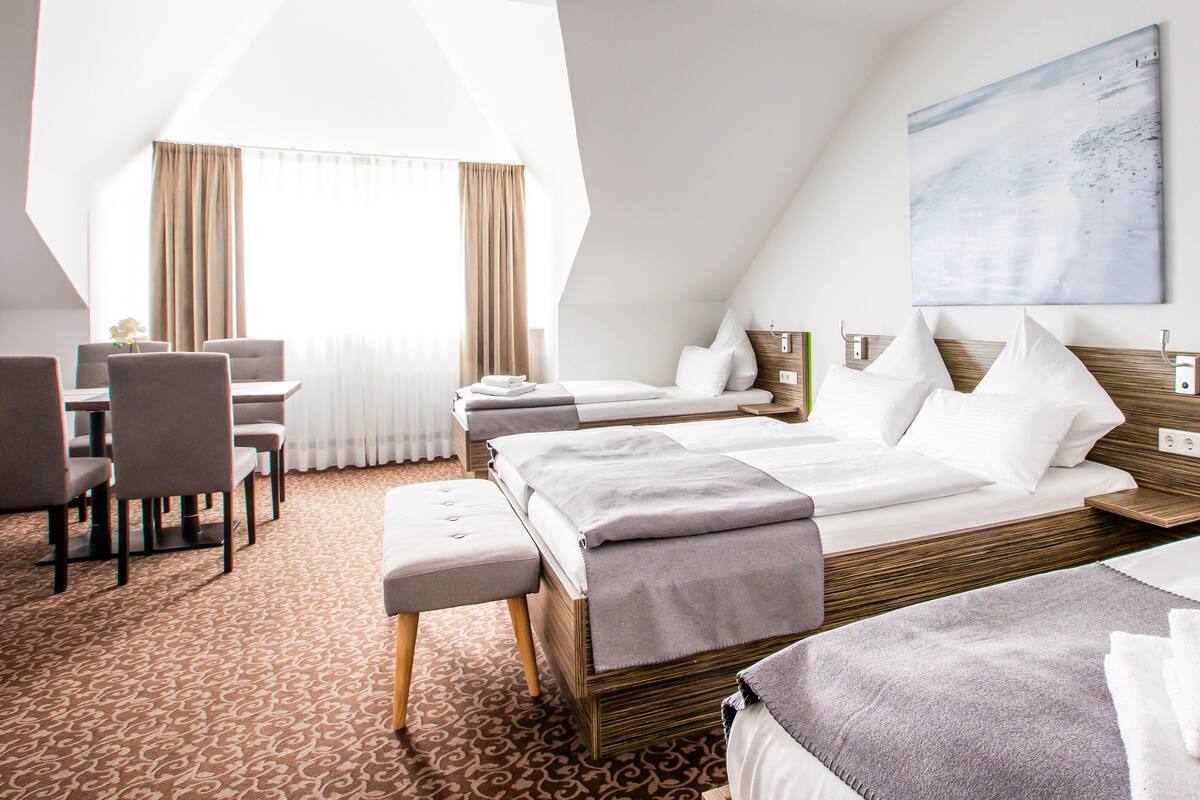 A hotel room with a large bed, a smaller bed, a desk with chairs, and a large window with curtains.