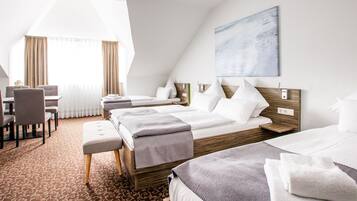 A hotel room with a large bed, a smaller bed, a desk with chairs, and a large window with curtains.