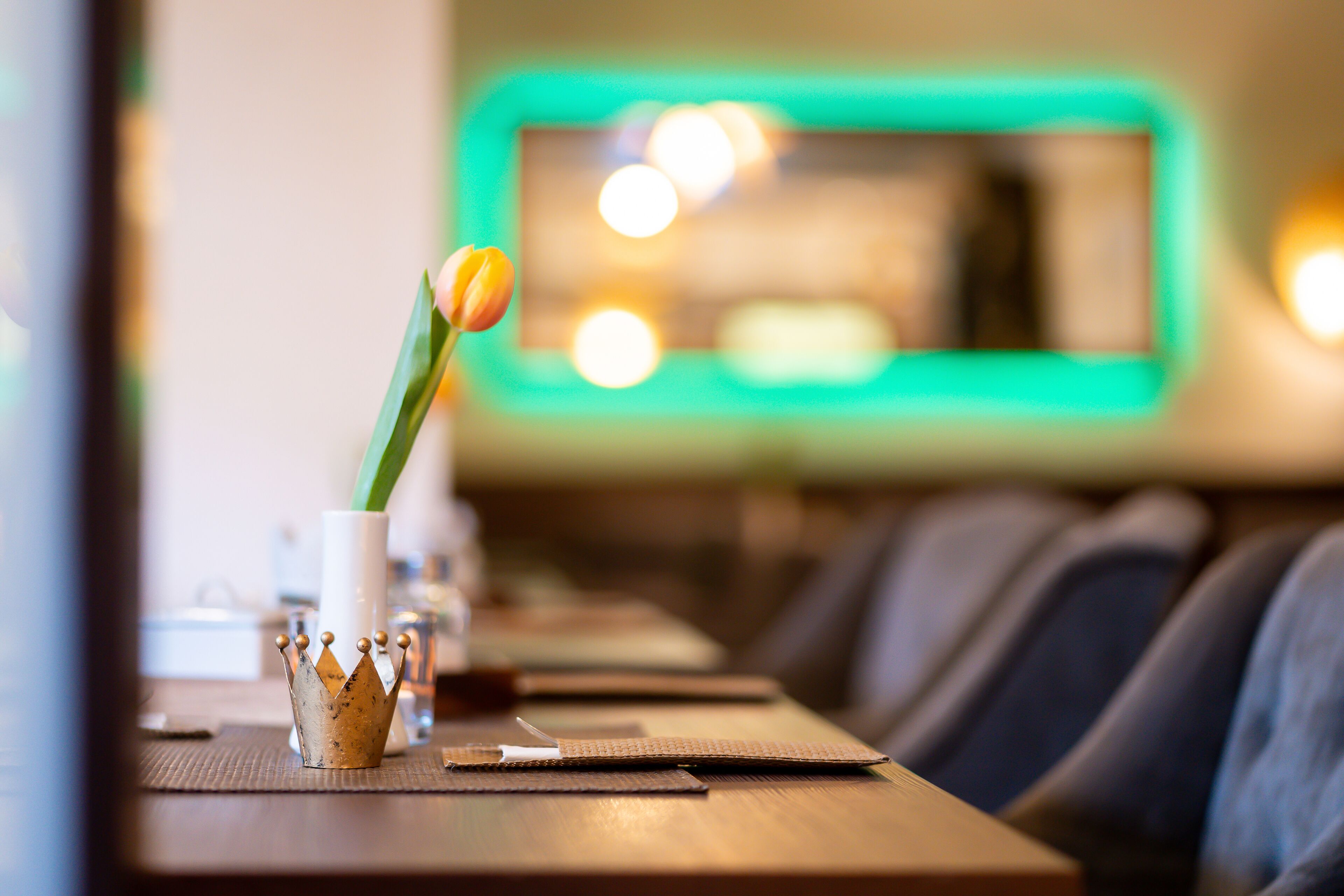 A restaurant interior with a long table, a decorative crown centerpiece, and a green-lit wall in the background.