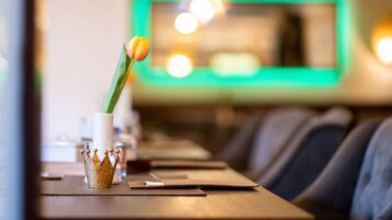 A restaurant interior with a long table, a decorative crown centerpiece, and a green-lit wall in the background.