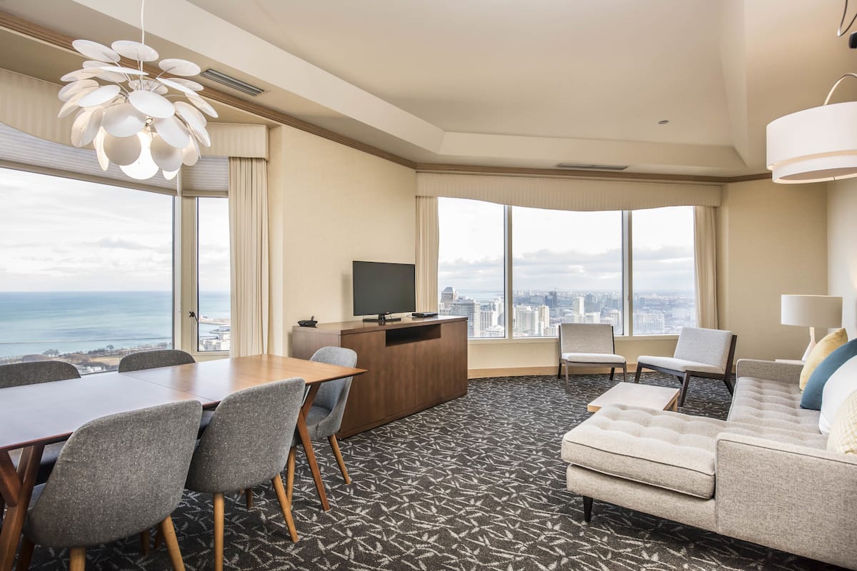 A hotel room with a city view, a dining area, a sofa, and a TV.