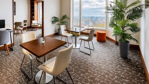 A modern hotel room with a city view, a dining area with a table and chairs, and a large potted plant. - The Buckingham Hotel (Chicago)