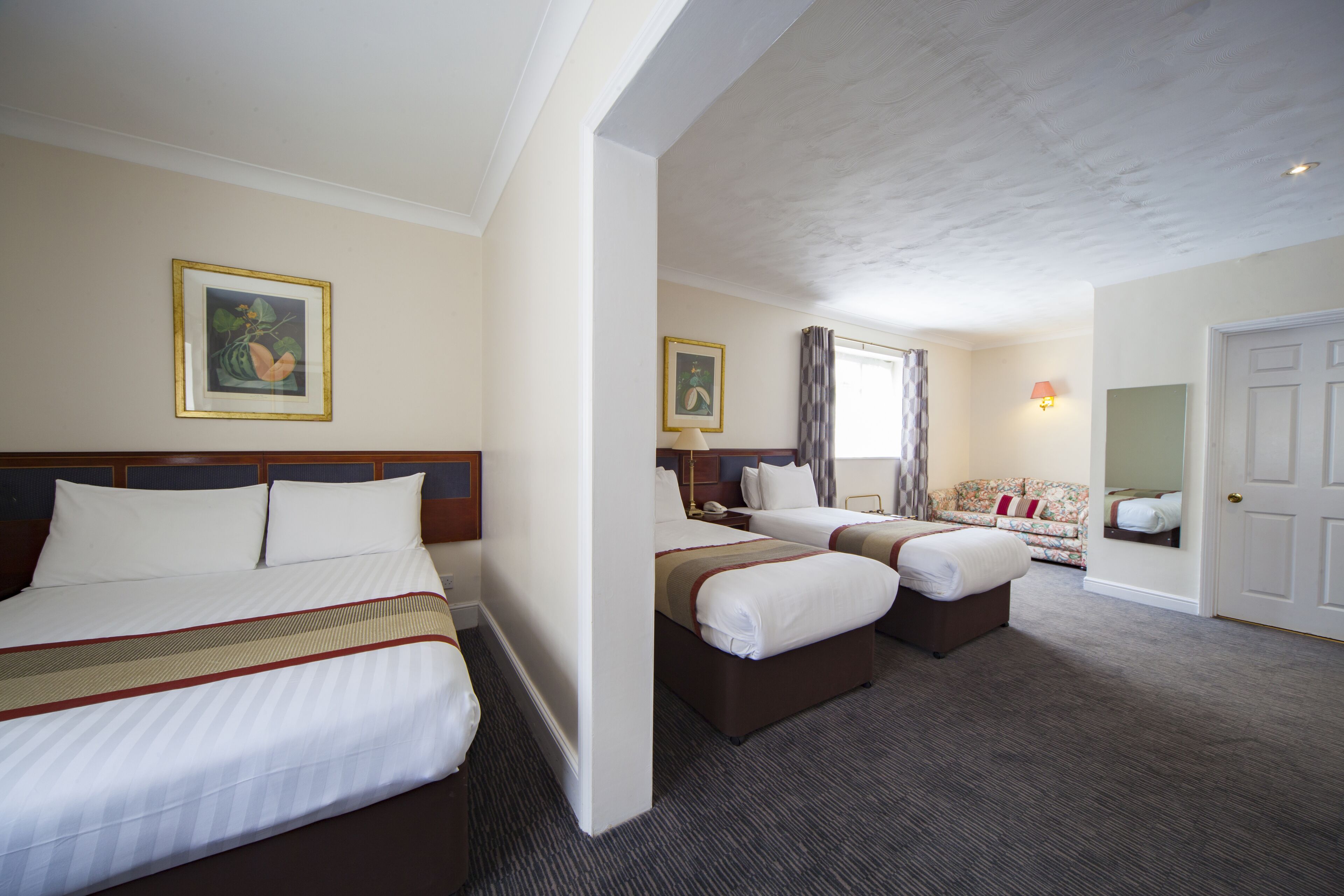 Habitación de hotel con dos camas, un sofá, una lámpara y un cuadro en la pared.
