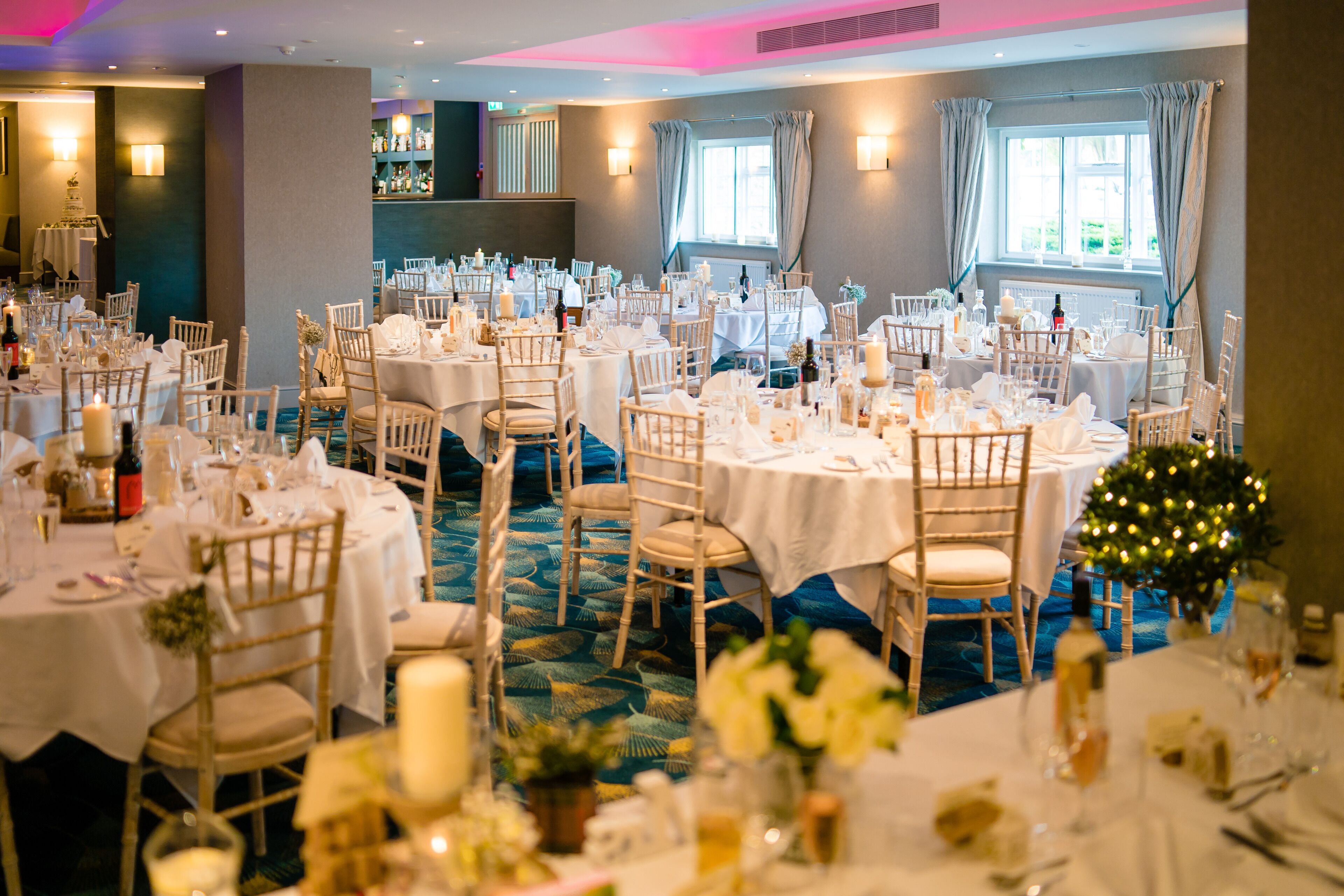 A banquet hall with round tables set for a formal event, featuring white tablecloths and floral centerpieces.