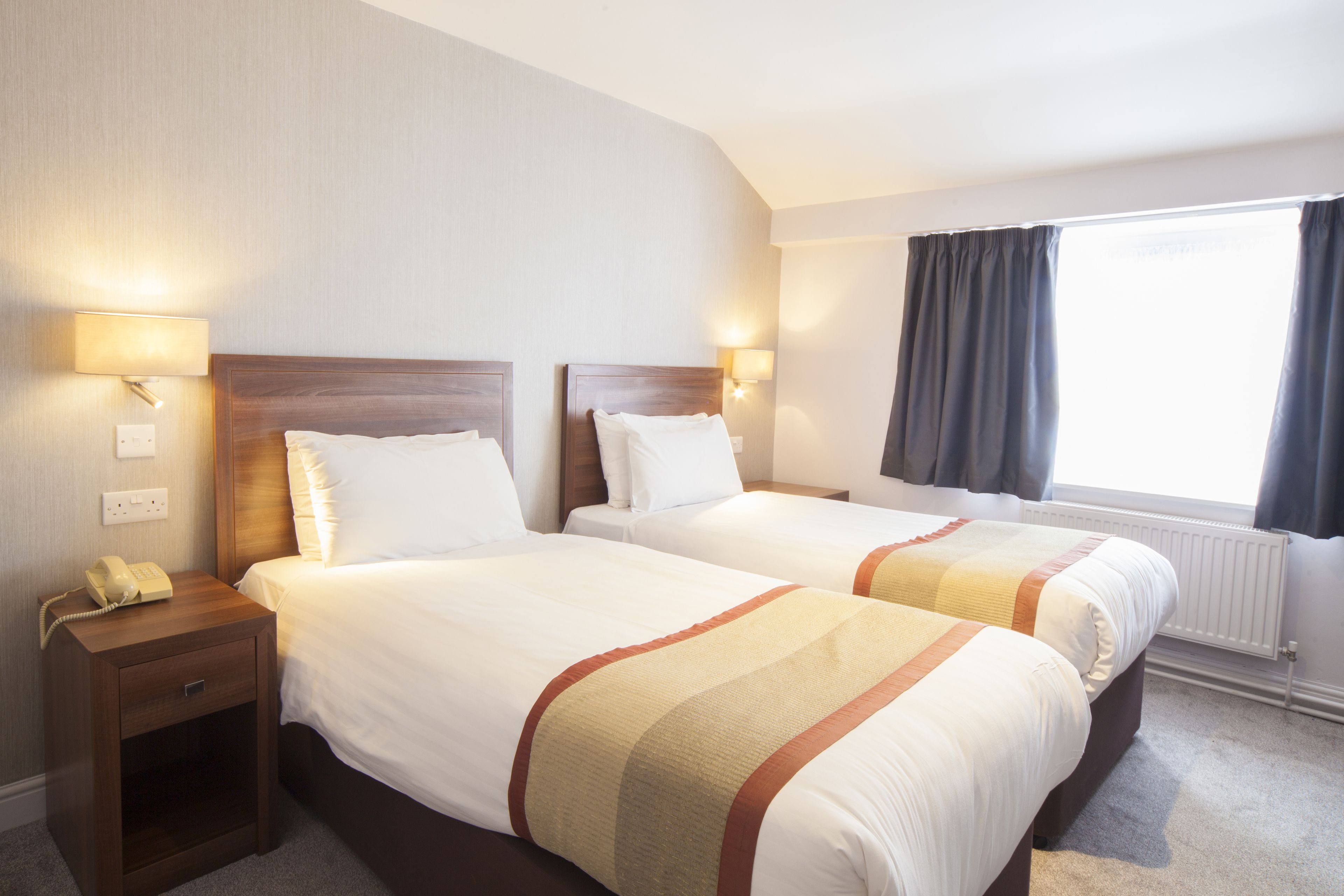 Een hotelkamer met twee bedden, bedlampjes, een nachtkastje en een raam met gordijnen.