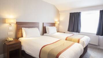 Een hotelkamer met twee bedden, bedlampjes, een nachtkastje en een raam met gordijnen.