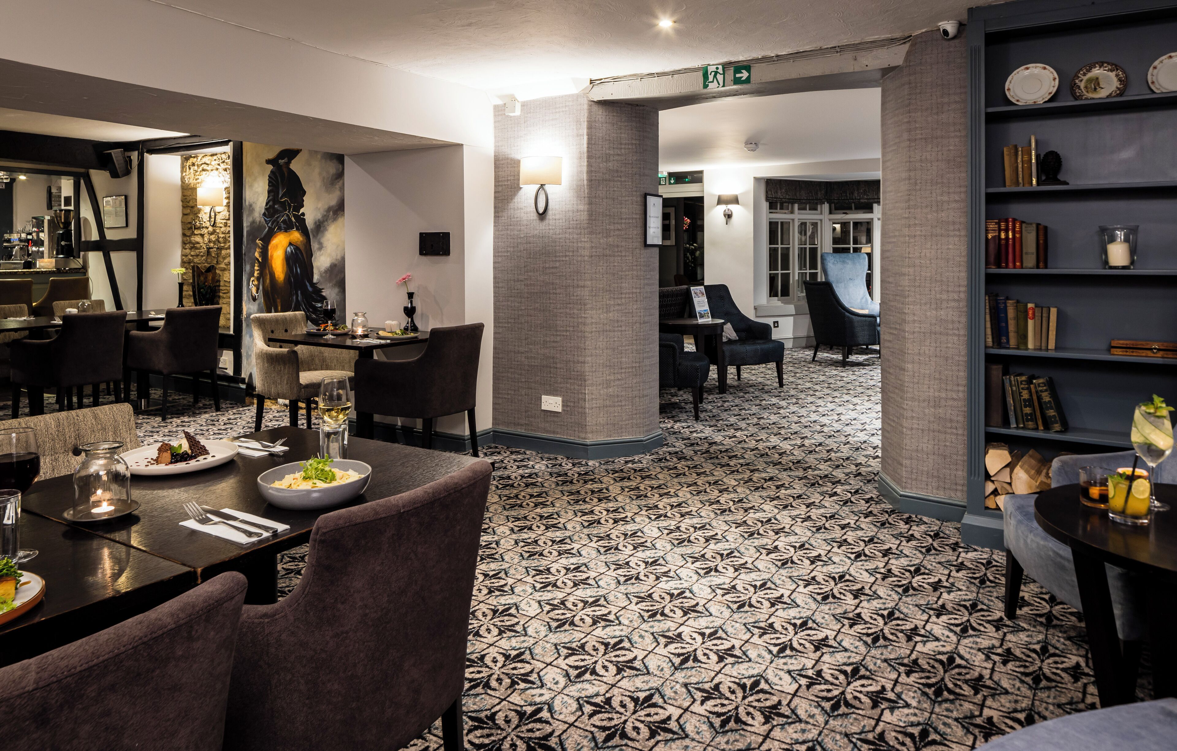 A hotel lobby with a patterned floor, a bar area, and a bookshelf with books and decorative items.