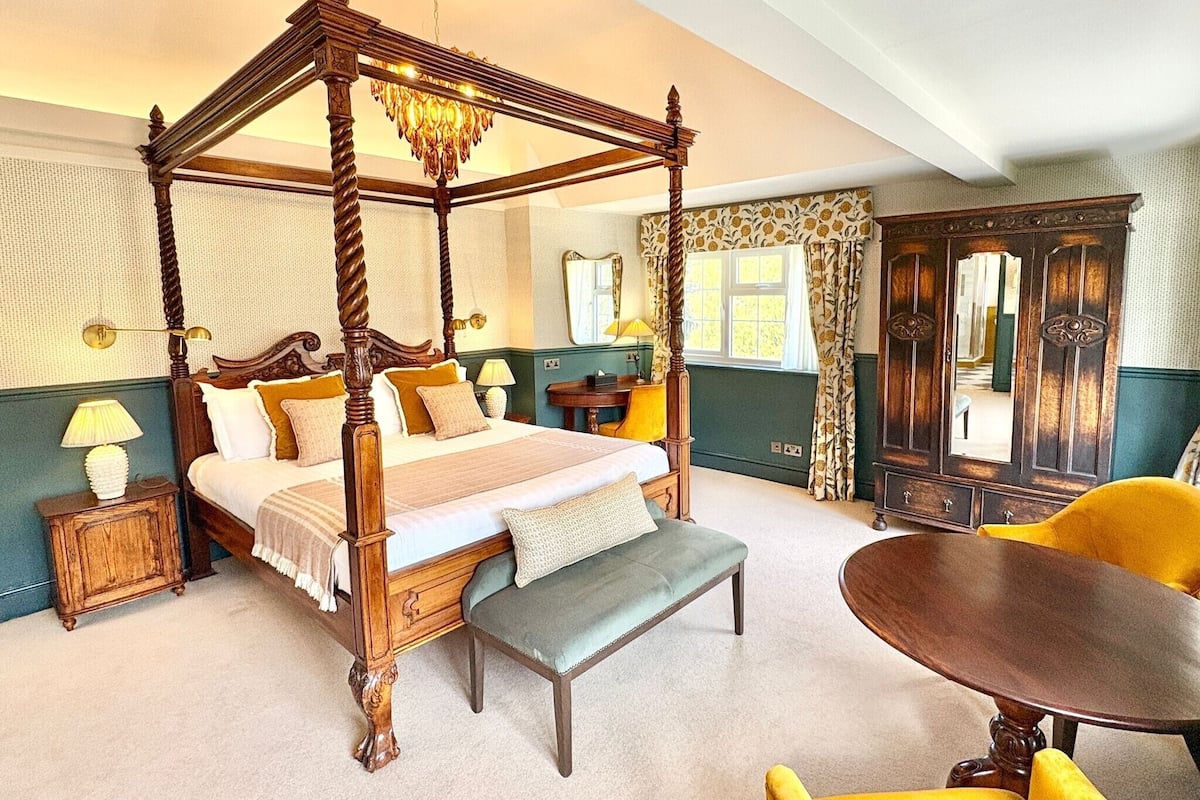 A four-poster canopy bed with a bench, a round table, and a mirror.