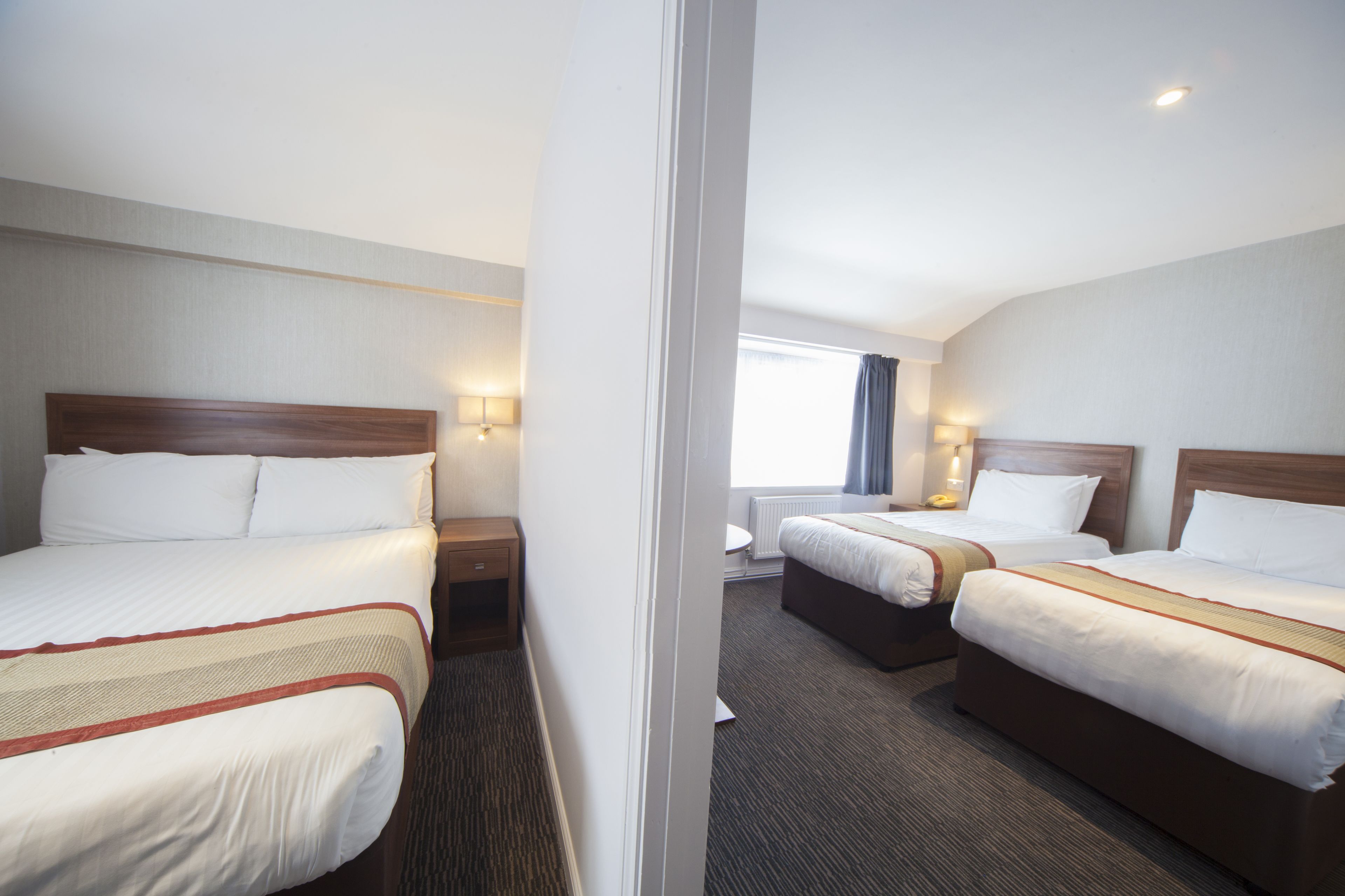 A hotel room with two beds, a window with curtains, and a nightstand with a lamp.