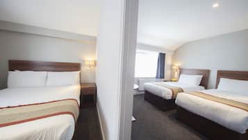 Een hotelkamer met twee bedden, een raam met gordijnen en een nachtkastje met een lamp.