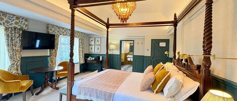 A four-poster bed with a chandelier, a television, and a desk with a chair in a hotel room.