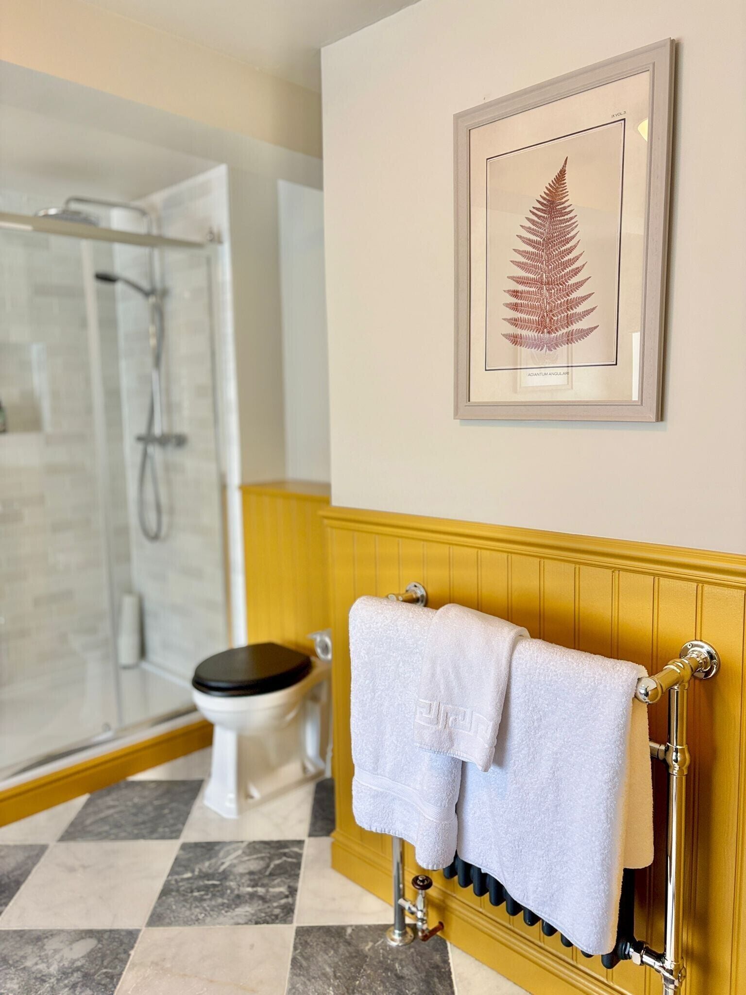 A bathroom with a shower, toilet, and a framed fern on the wall.