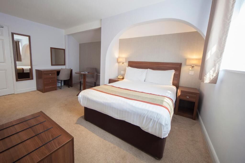 Une chambre d’hôtel avec un grand lit, un bureau, une chaise, une armoire et un miroir.