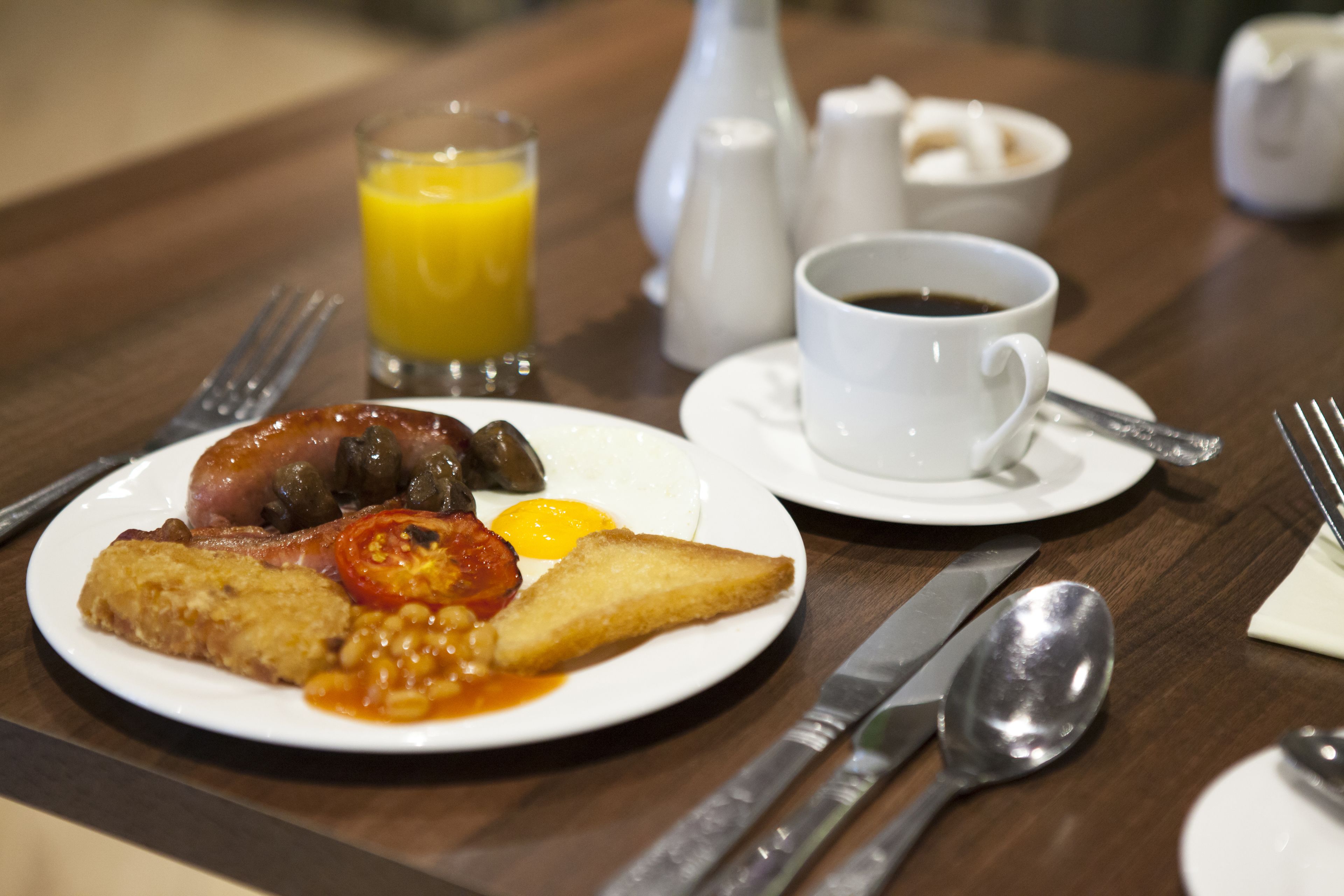Une assiette de petit-déjeuner avec des œufs, du bacon, des tomates, des haricots et des toasts, posée sur une table en bois.