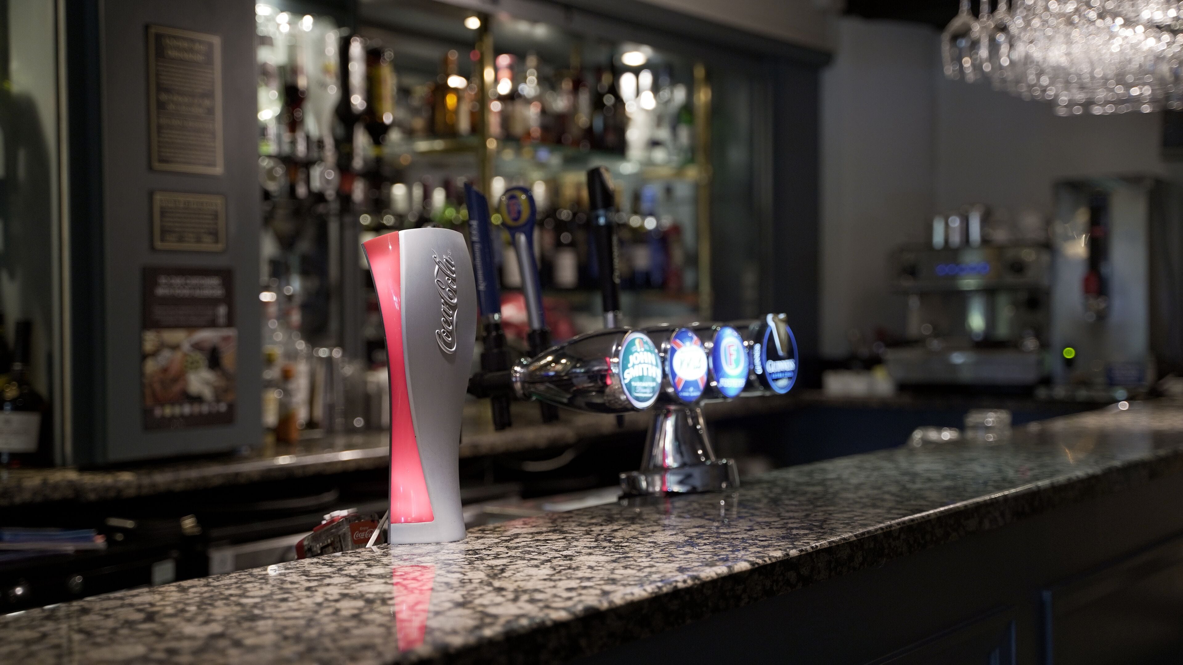 A bar counter with a tap labeled "Coca-Cola" and several beer taps with different brands.