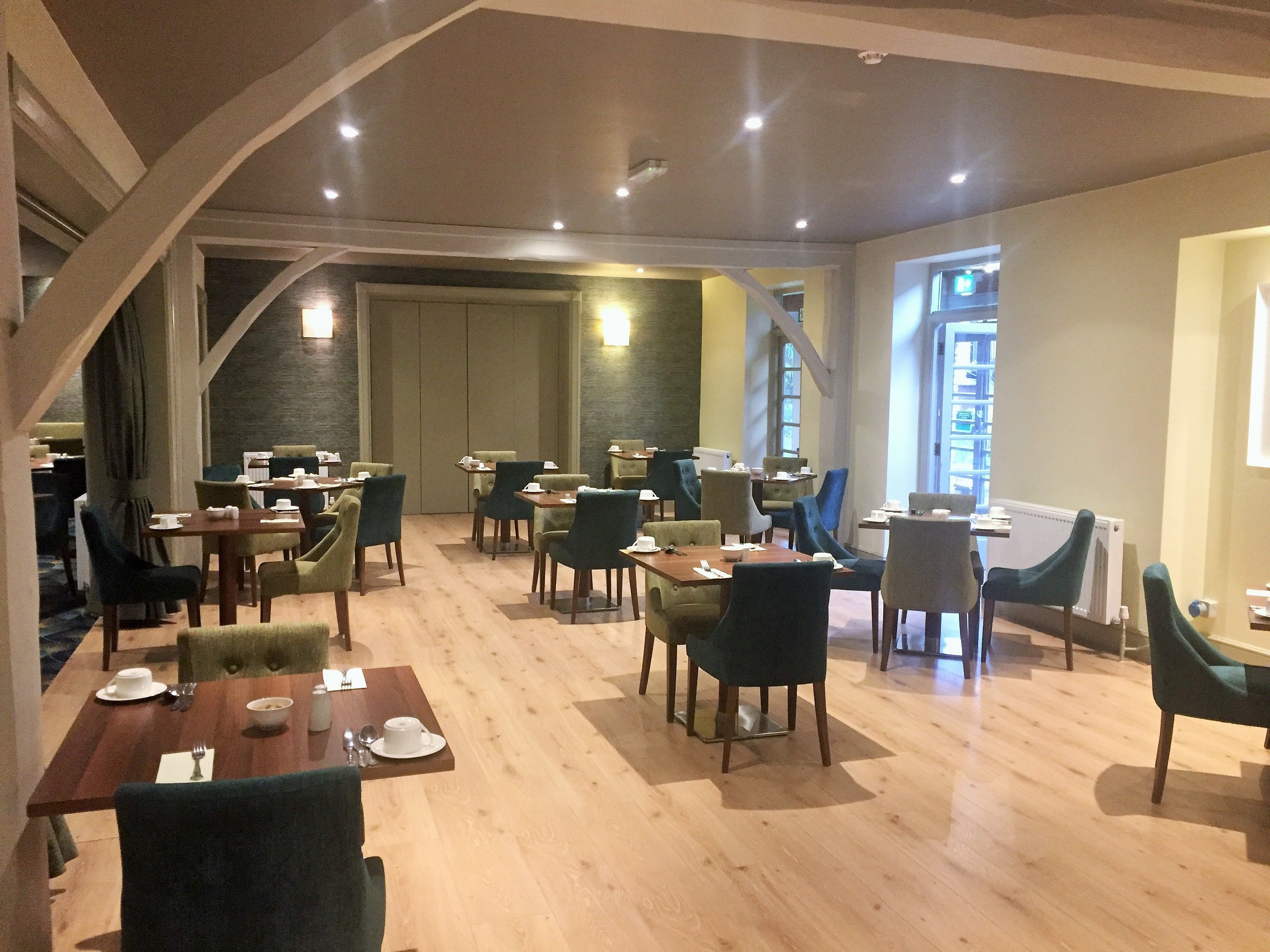 A restaurant with wooden tables and chairs, a high ceiling, and a view of the outside.