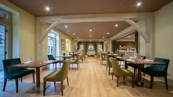 A spacious dining area with multiple tables and chairs, wooden flooring, and a view of the kitchen in the background.