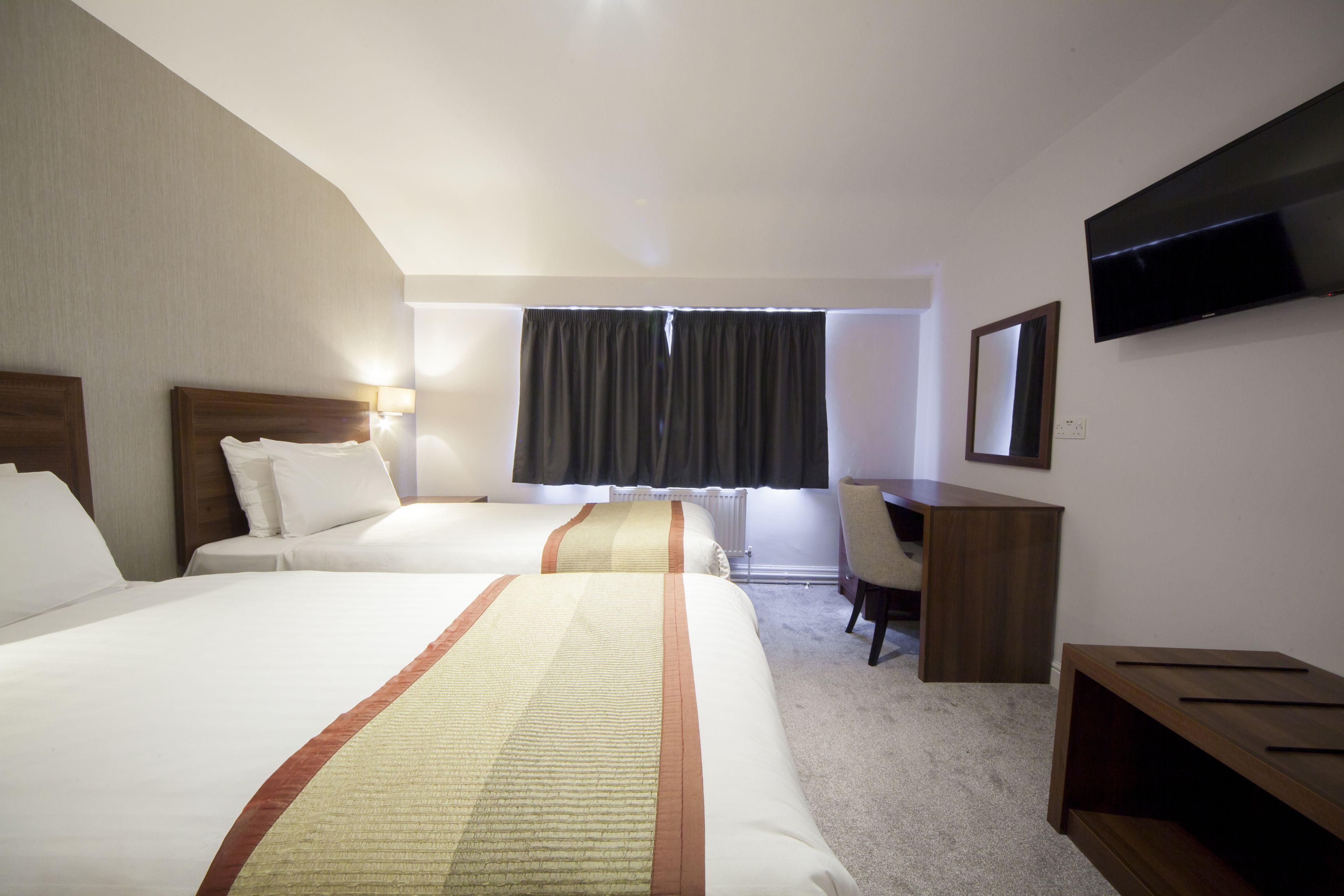Habitación de hotel con dos camas, un escritorio, una silla, un televisor y una ventana con cortinas.