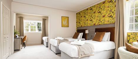Habitación de hotel con una cama grande, un escritorio y una silla. Hay una ventana con cortinas, una pared con papel tapiz floral y un cuadro en la pared.