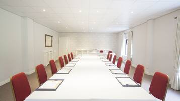 Un salón de conferencias con una larga mesa, sillas rojas y un mantel blanco.