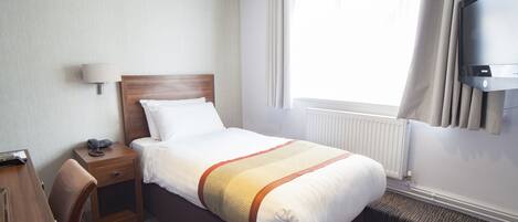 A hotel room with a bed, a desk, a chair, a lamp, a TV, and a window with curtains.