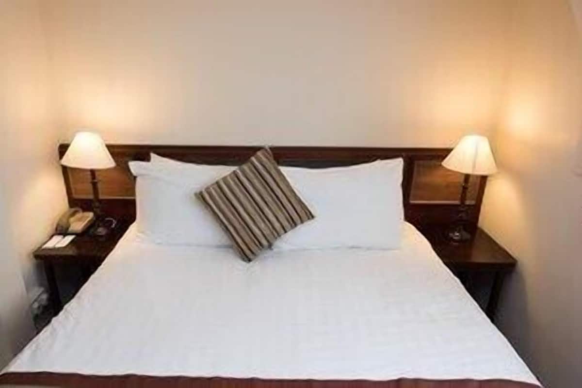 A hotel room with a bed, two bedside lamps, a telephone, and a pillow.