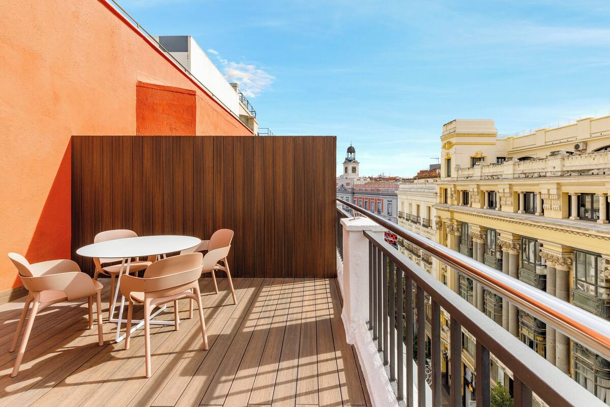 Ein Balkon mit Holzboden, einem weißen runden Tisch und vier Stühlen.