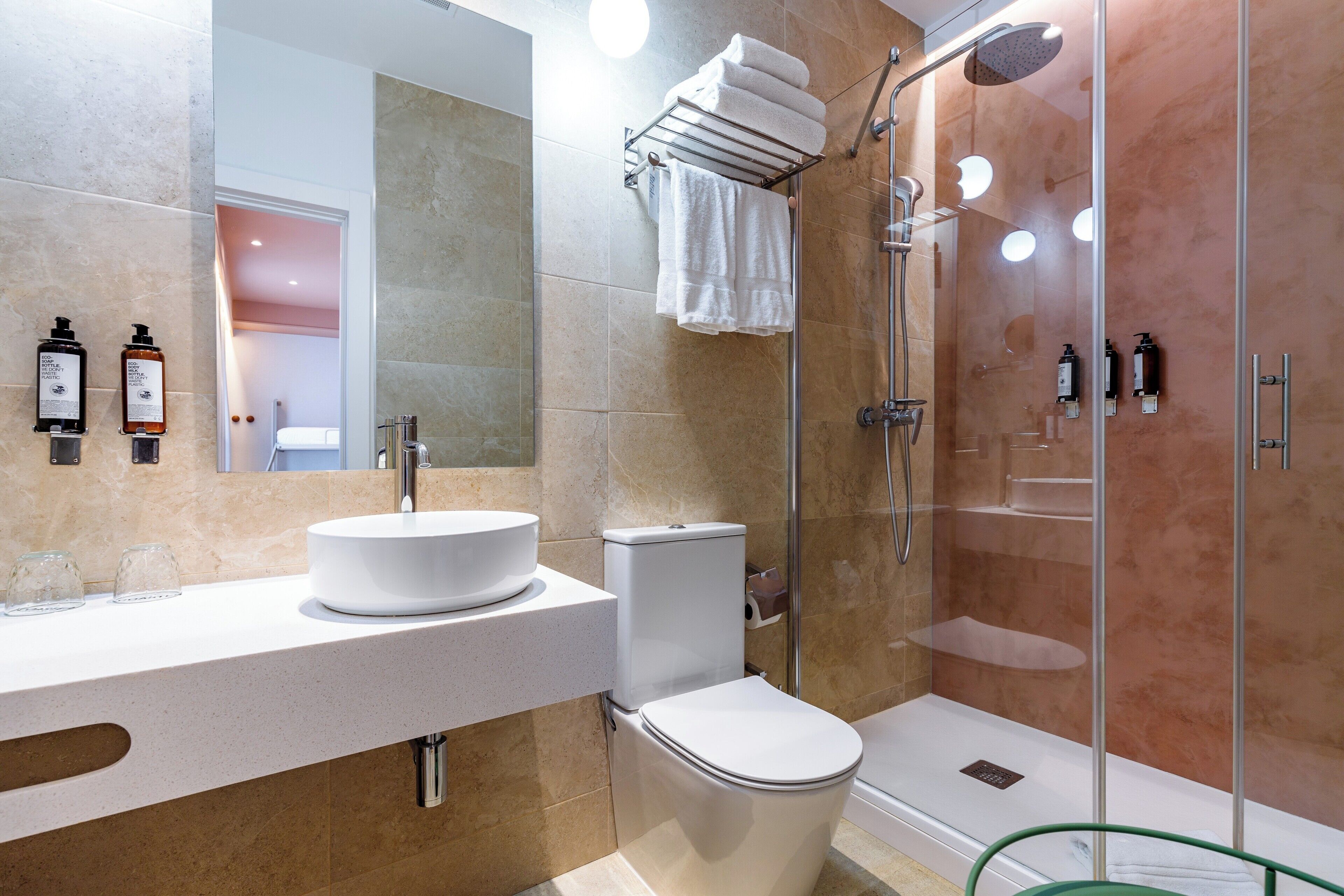 A modern bathroom with a round sink, toilet, and glass-enclosed shower.