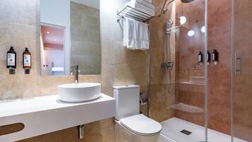 A modern bathroom with a round sink, toilet, and glass-enclosed shower.