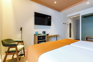 Ein modernes Hotelzimmer mit Bett, Schreibtisch, Stuhl, Flachbildfernseher und einer kleinen Küchenzeile.