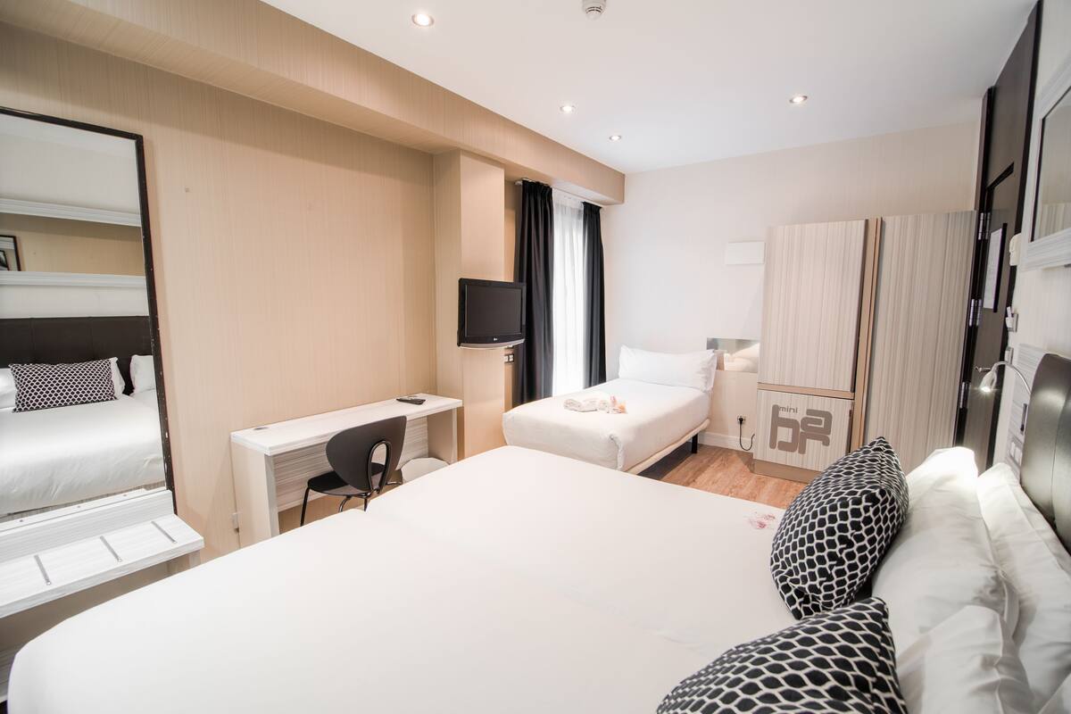 Ein Hotelzimmer mit Bett, Schreibtisch, Stuhl, Fernseher, Kleiderschrank und Spiegel.