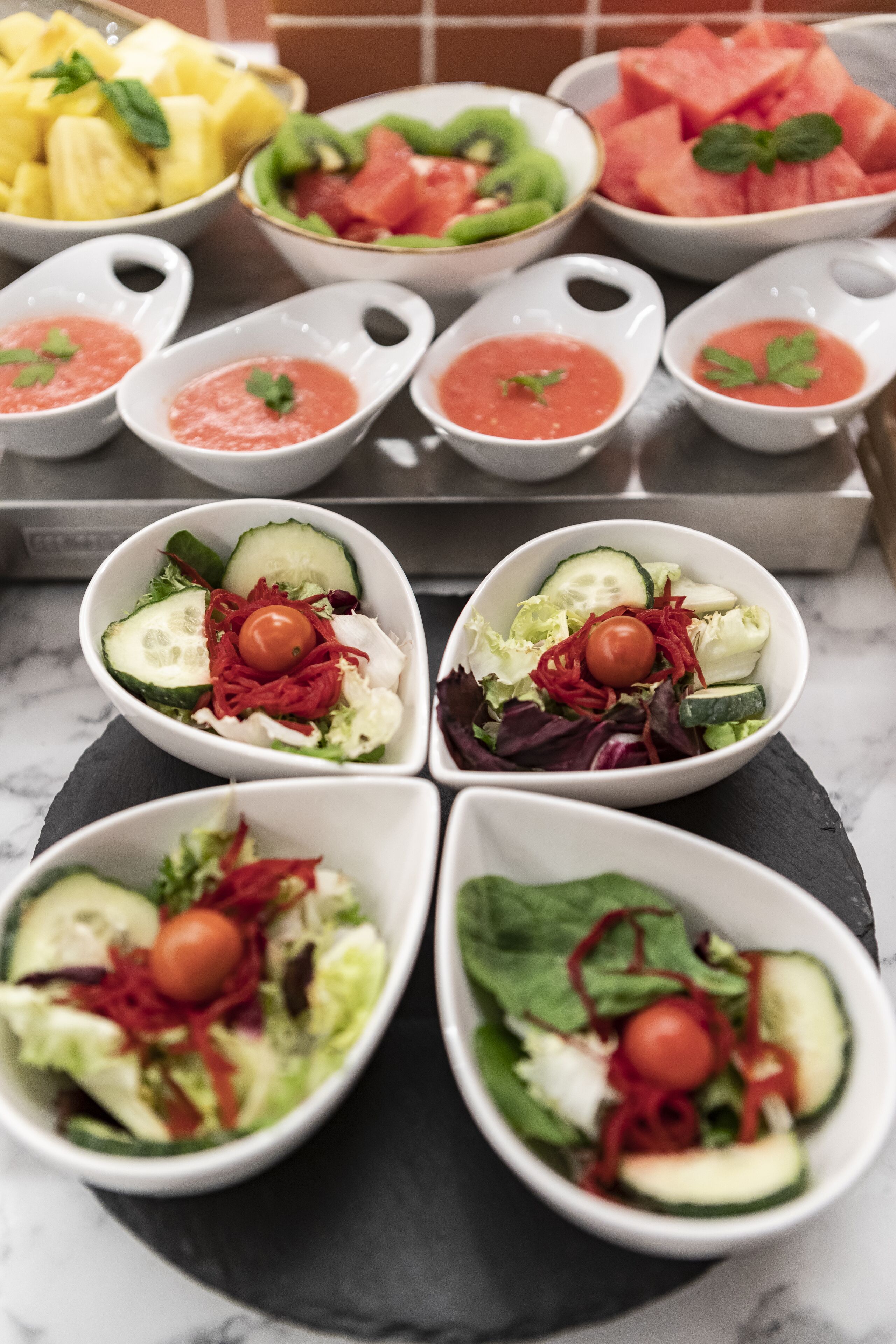 Diversos cuencos de fruta y ensaladas sobre una encimera de mármol.
