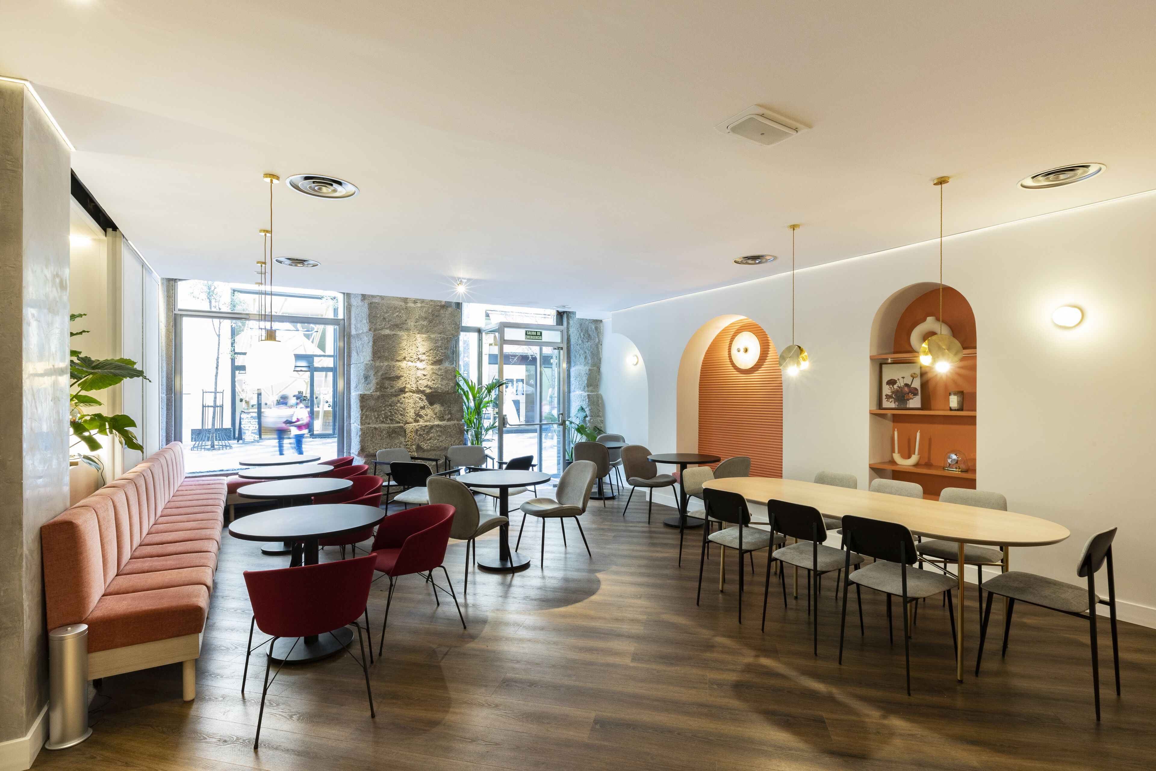 Een moderne eethoek met een combinatie van ronde en rechthoekige tafels, rode en grijze stoelen en een lange bank.