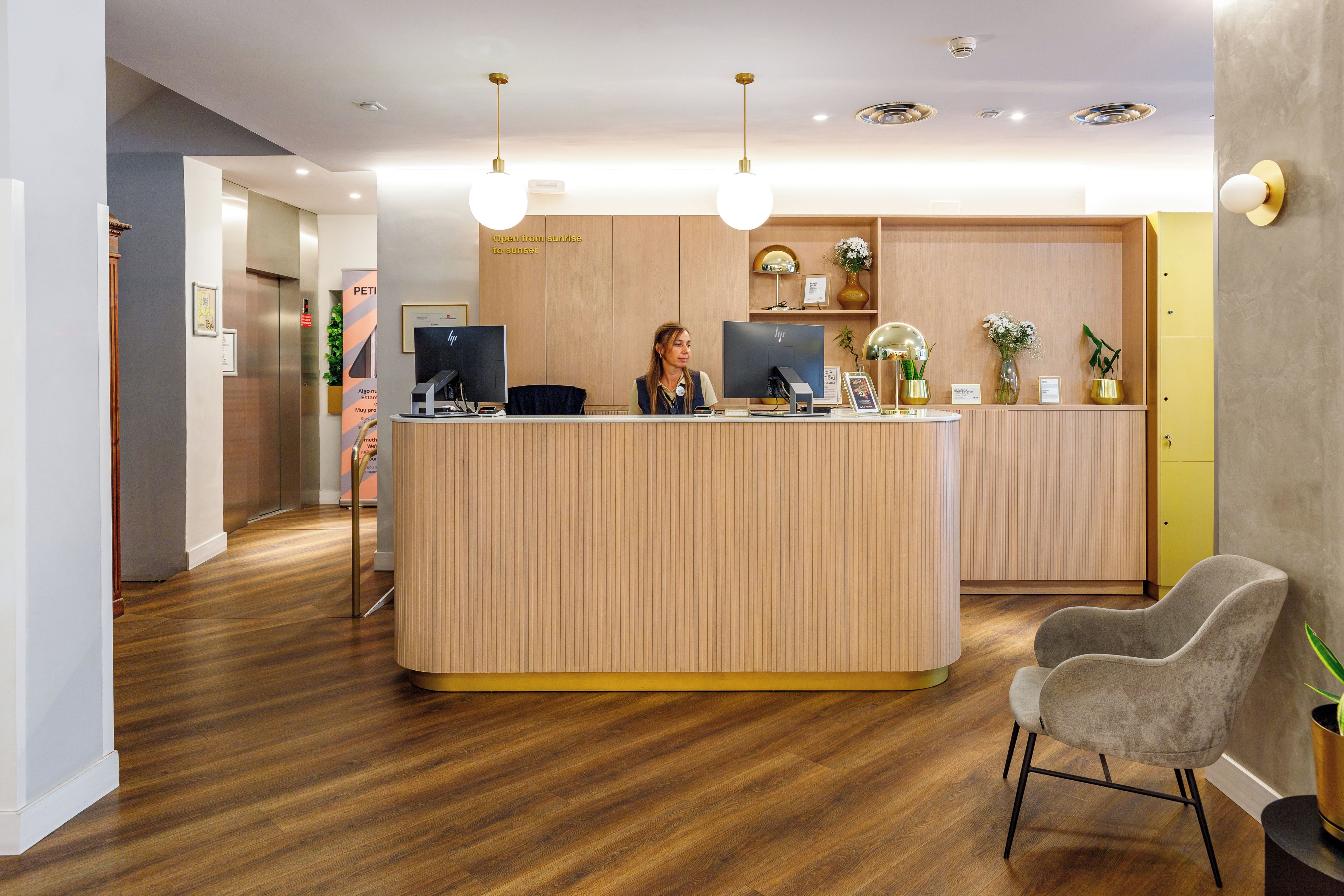 A reception desk with a receptionist, a wooden floor, and a grey chair.