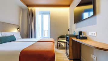 A hotel room with two beds, a desk, a chair, a television, and a window with curtains.