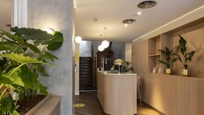 Zona de recepción con mostrador de madera, plantas en macetas y una escalera al fondo.
