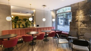 Una cafetería moderna con pared de piedra, mesas redondas, sillas rojas y lámparas colgantes.
