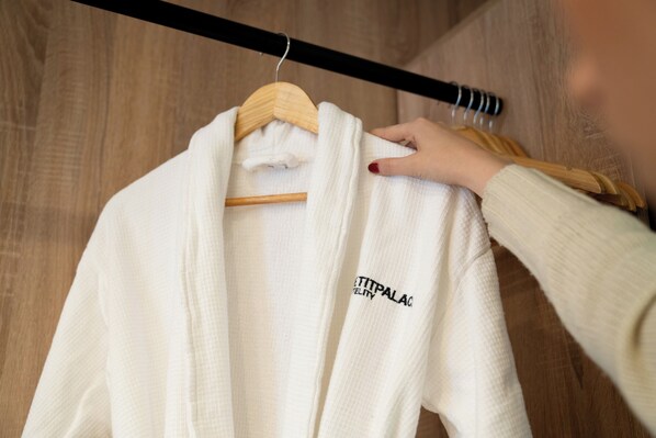 A white robe hanging on a wooden hanger in a room with wooden flooring. - Petit Palace Puerta del Sol (Madrid)