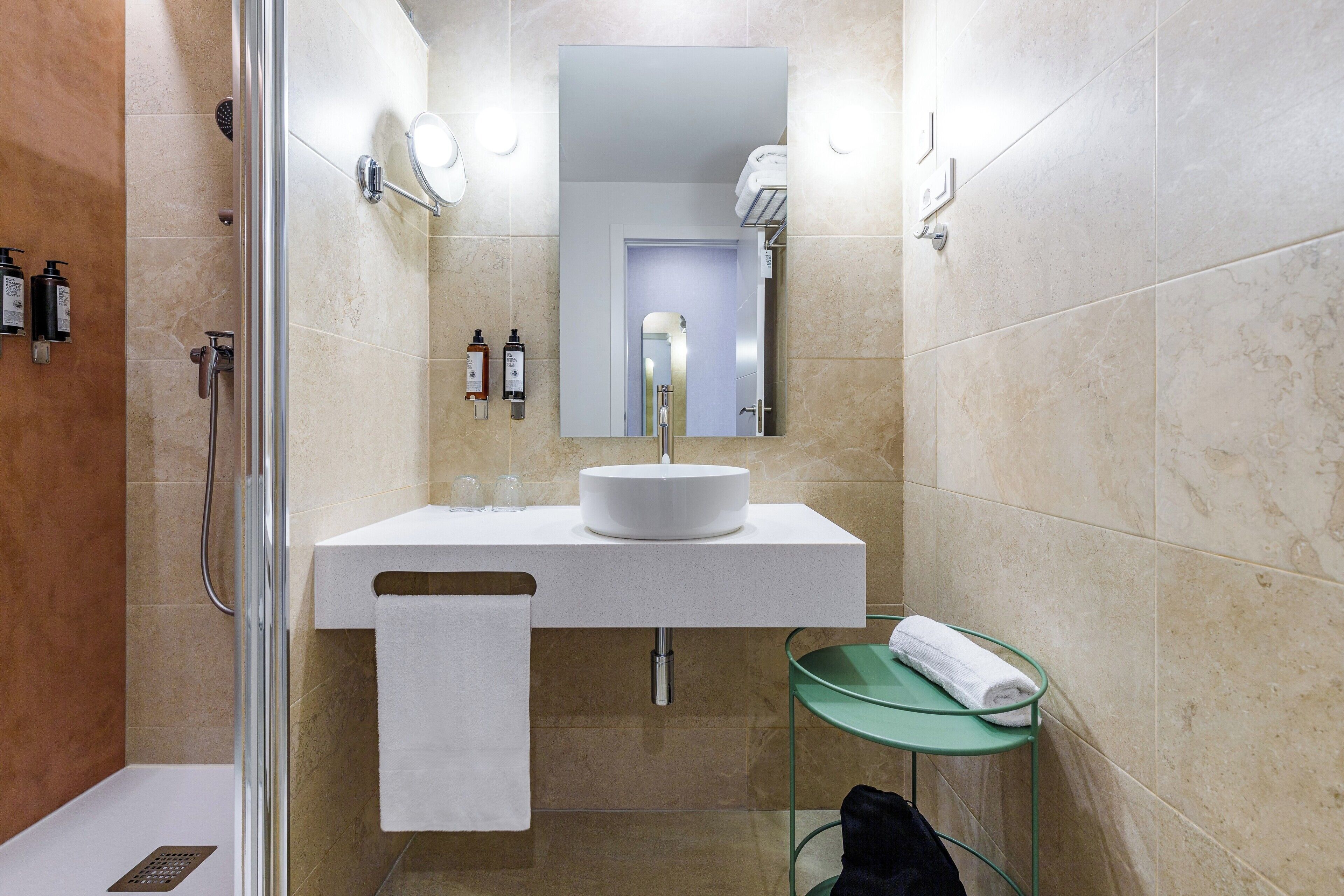 A modern bathroom with a glass shower enclosure, a white sink with a mirror above it, and a glass shelf with a towel.