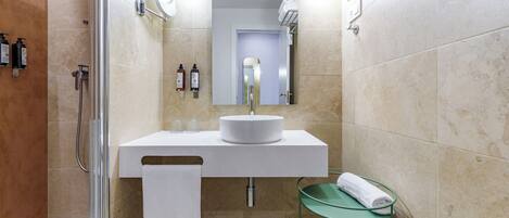 A modern bathroom with a glass shower enclosure, a white sink with a mirror above it, and a glass shelf with a towel.