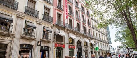 Un edificio histórico con varias tiendas, incluyendo una tienda de Real Madrid, y un llamativo cartel rojo.