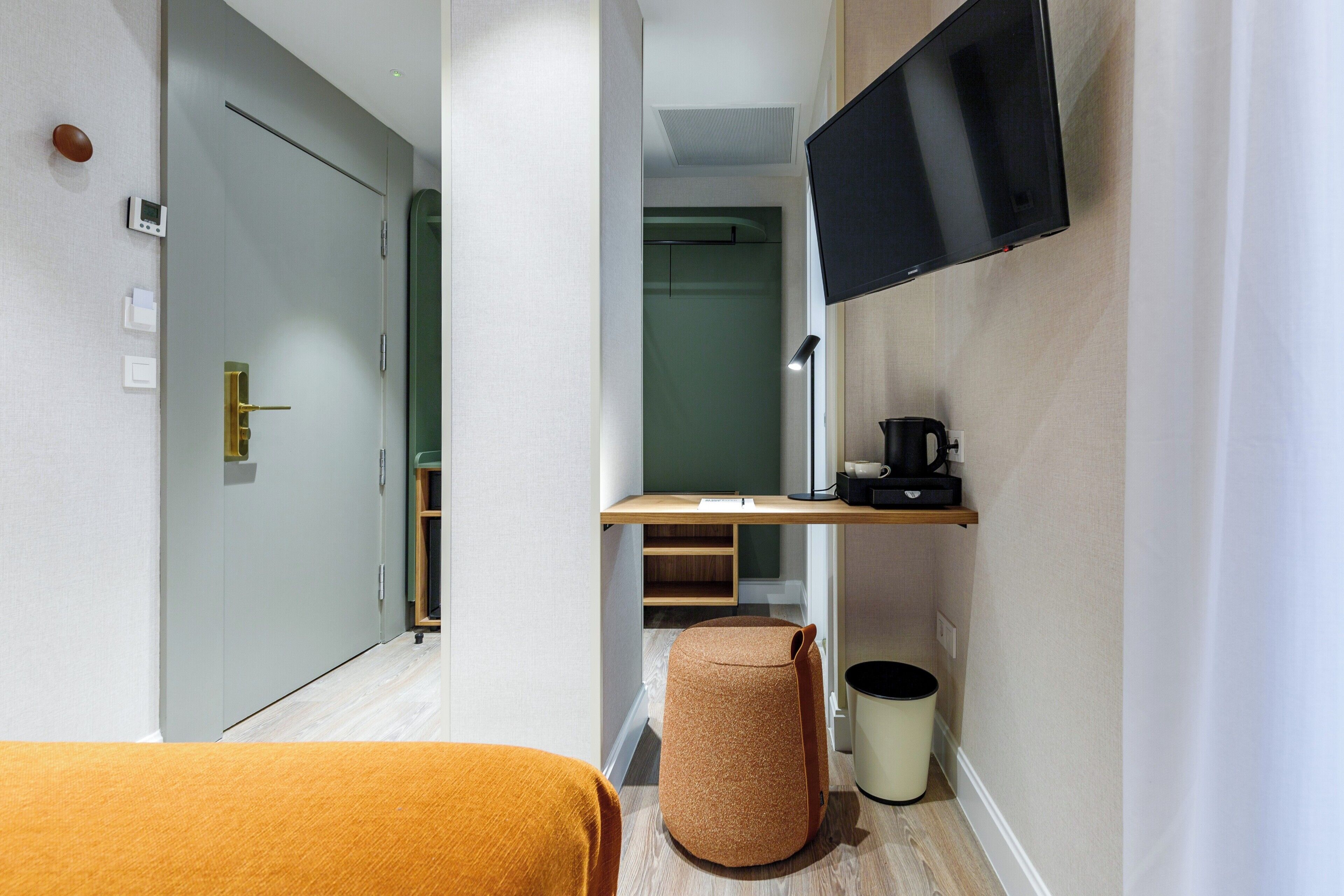 Una habitación de hotel moderna con una cama, un televisor montado en la pared, un escritorio pequeño con una cafetera y un cubo de basura.