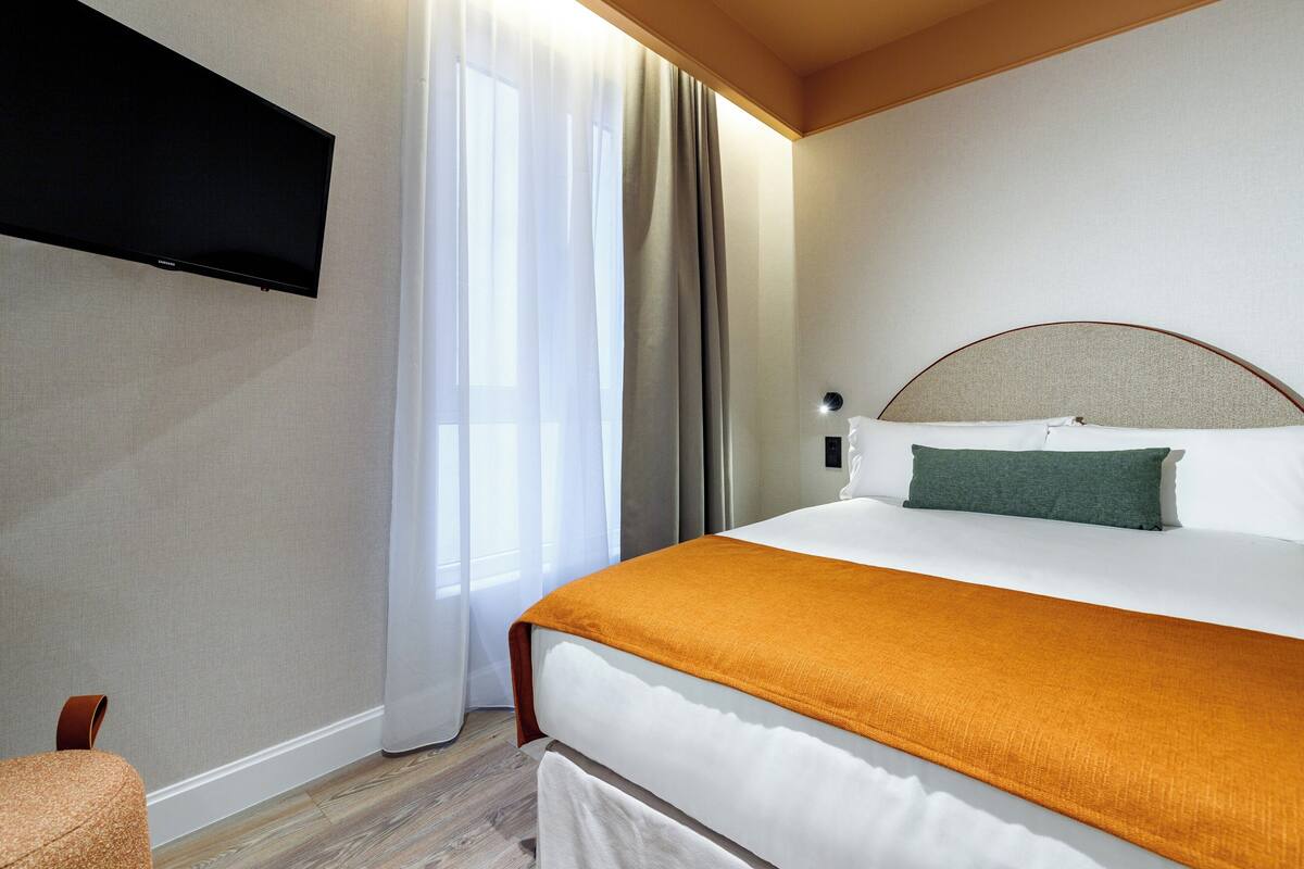 Ein Hotelzimmer mit Bett, Flachbildfernseher an der Wand, einem Fenster mit Vorhängen und Holzboden.