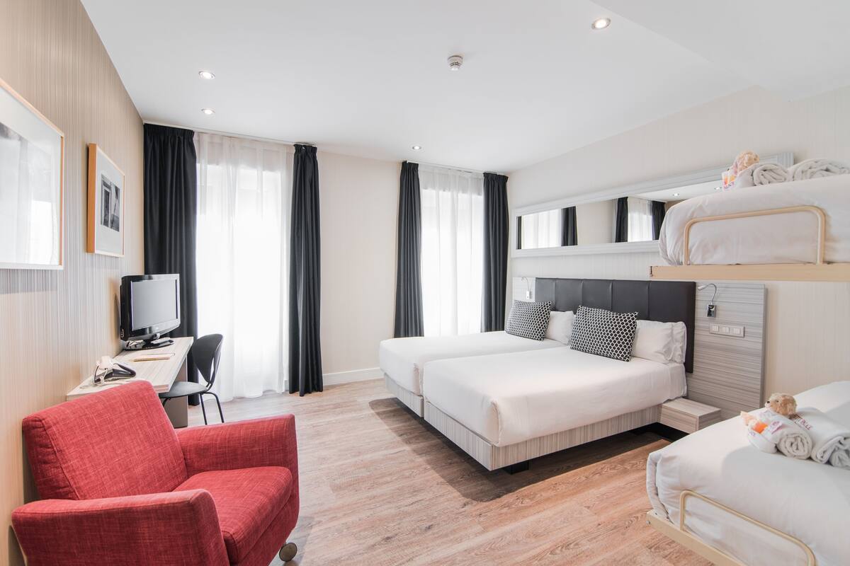 Ein Hotelzimmer mit einem Bett, einem Schreibtisch mit Computer, einem roten Sessel und einem Stockbett.