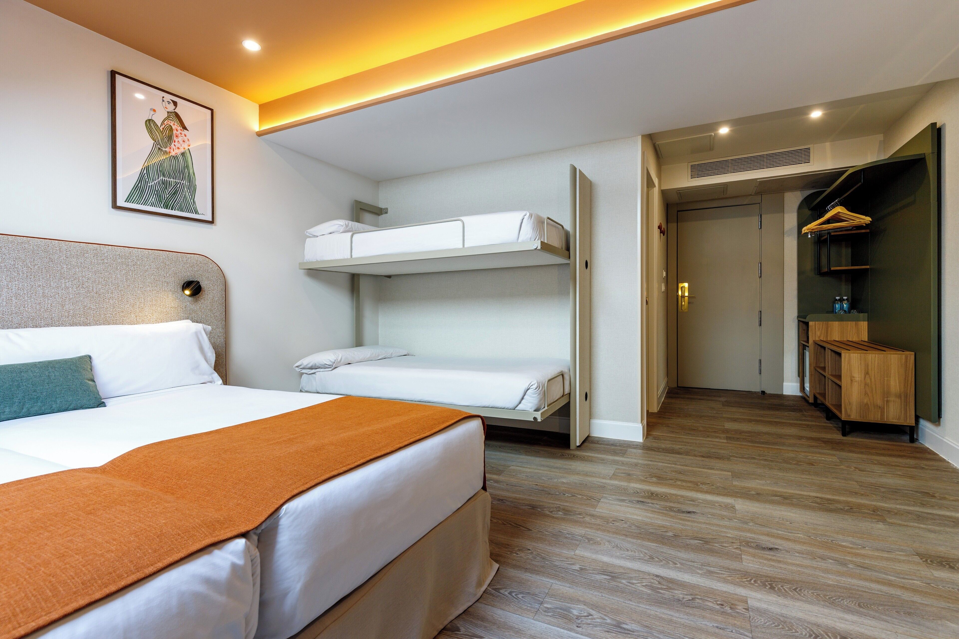 A hotel room with a large bed, a bunk bed, a wardrobe, and a framed picture on the wall.